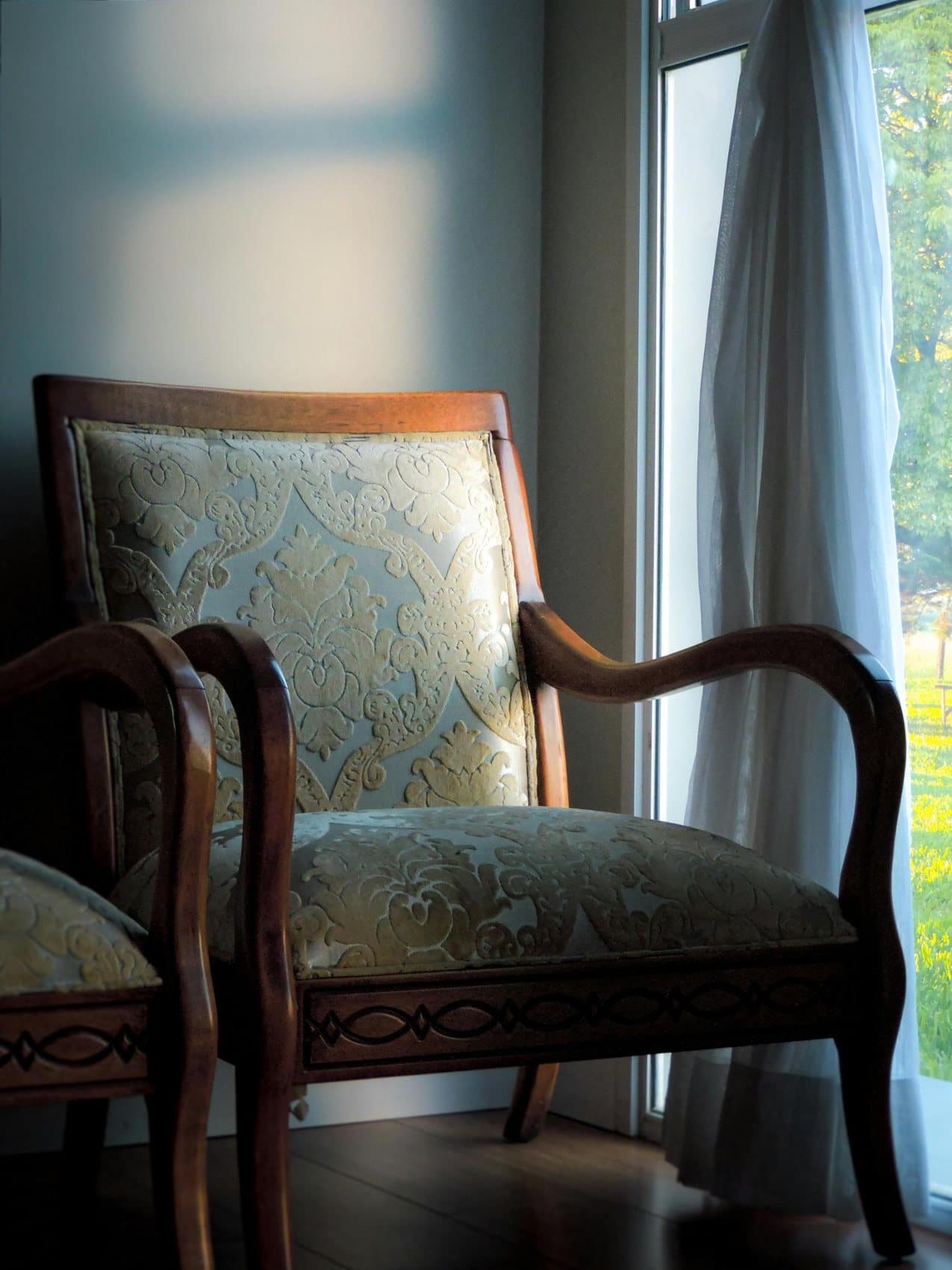 Antique armchair reupholstered in a patterned damask, beside a sunlit window